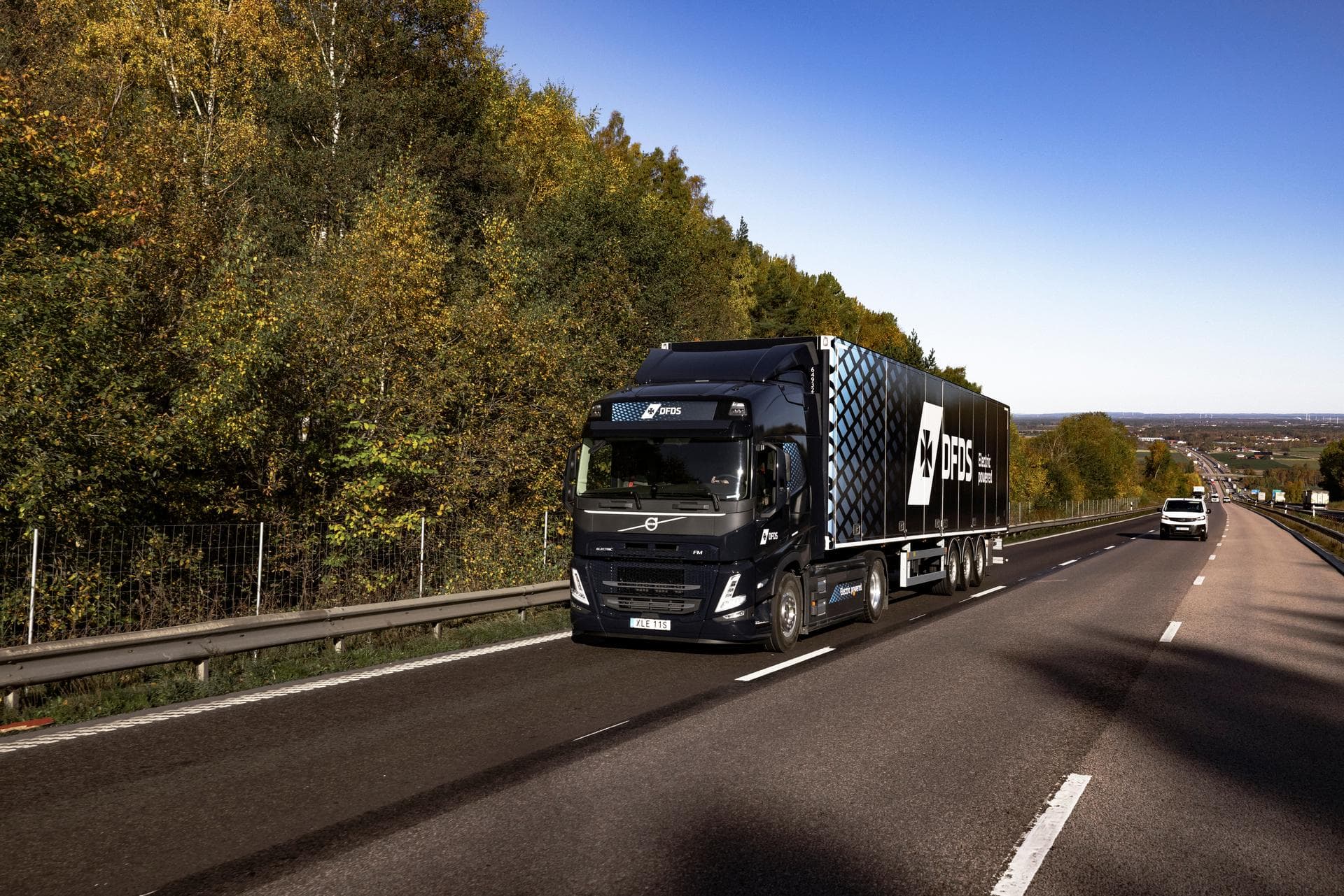 A DFDS-branded Volvo electric truck drives past trees on a highway