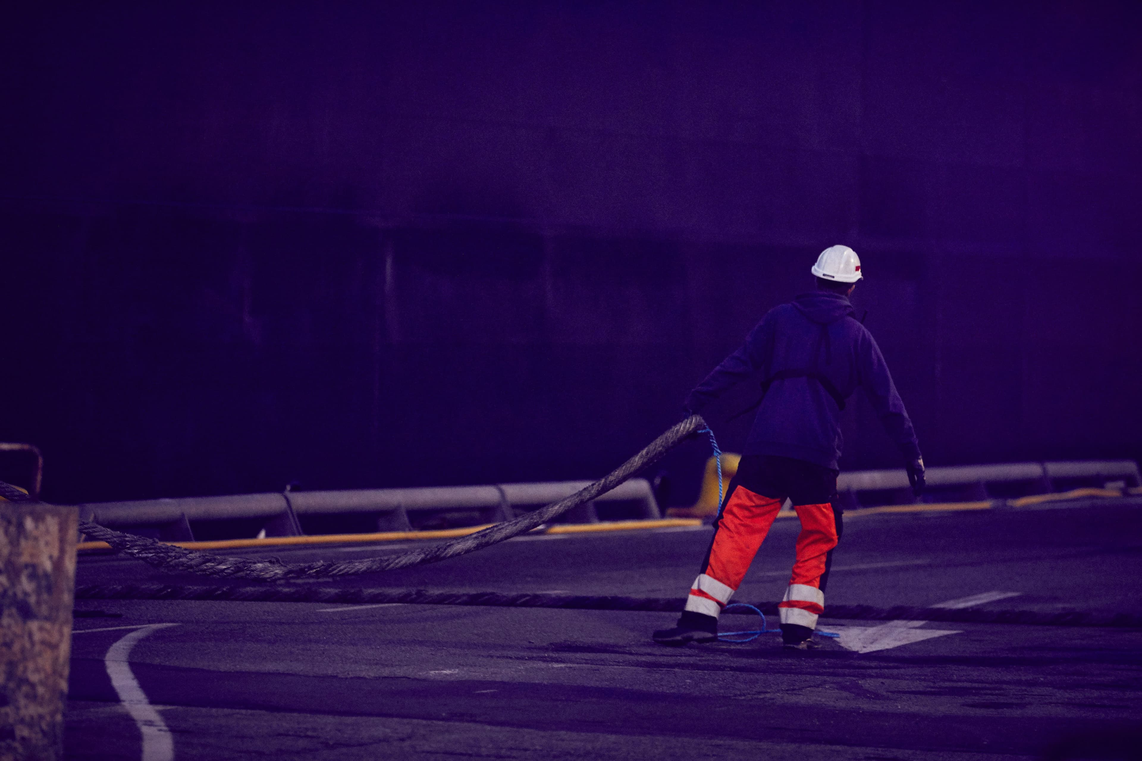 Terminal worker pulling a rope, next to a ship docked at port.