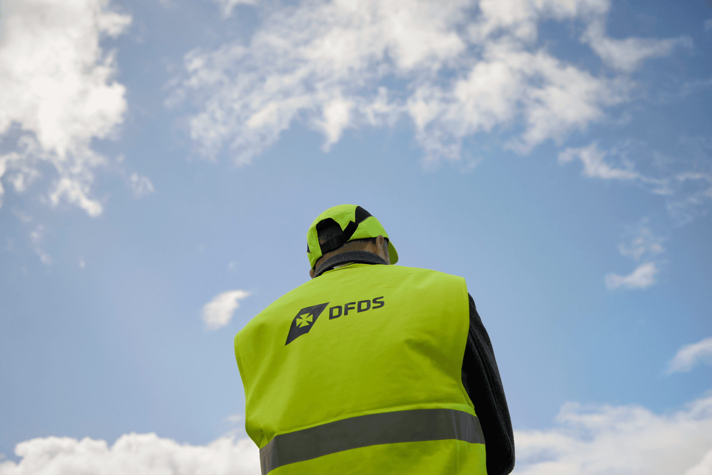 DFDS worker wearing a safety vest, with clouds in the background.